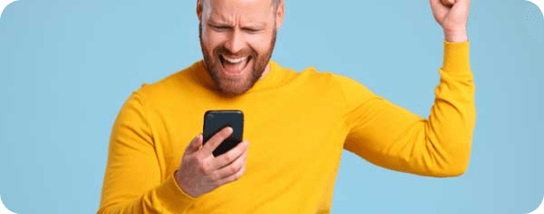 A happy man looking down at his phone, excited by what he is seeing.